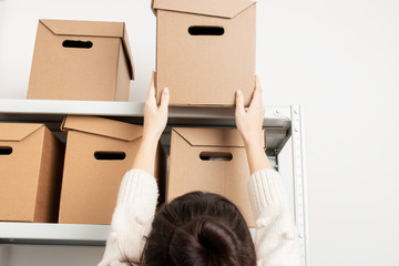 Woman take a cardboard box from a shelf of a rack in warehouse close up. Clean up and organize a pantry concept.