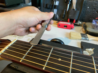guitar technician is measure the height of the guitar string to complete the set-up.