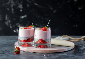 Chia seeds pudding with strawberry and banana in glasses on dark background, healthy tasty dessert....