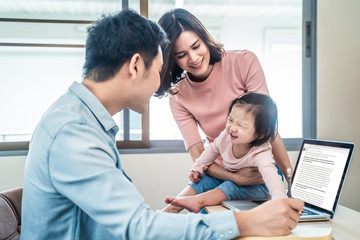 Obraz premium Asian young businessman happy to work on computer at home office, spending time with daughter, wife family. Man work from home during Coronavirus, Covid19 crisis outbreak, for prevent contract disease