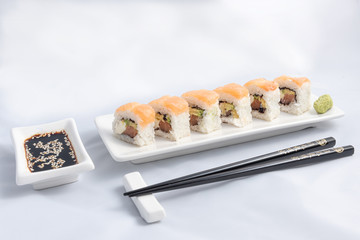Sushi roll with pink salmon wrap, grilled salmon, Philadelphia cheese and avocado. White container and black chopsticks.