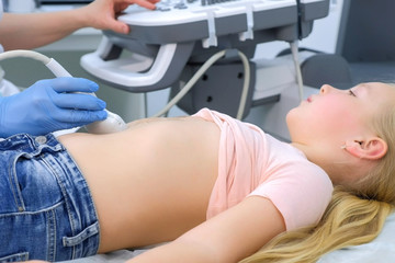 Doctor making abdominal ultrasound for child girl using scanner, closeup side view, tummy and hands closeup. Woman runs ultrasound sensor over patient belly. Diagnostic examination of internal organs.