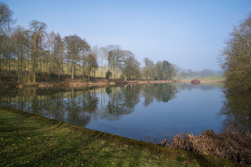 Fototapeta premium View of a lake in the English countryside on an autumn morning with reflected trees