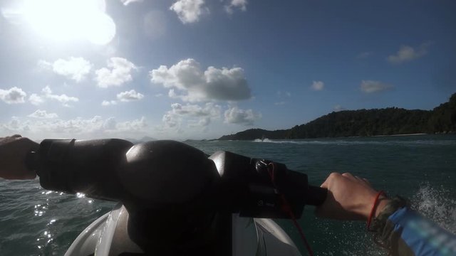 Young man rides water motorcycle and it's making waves and splashes. At the background there is a big island with huge green trees. Concept of travelling and vacational journey in Thailand.