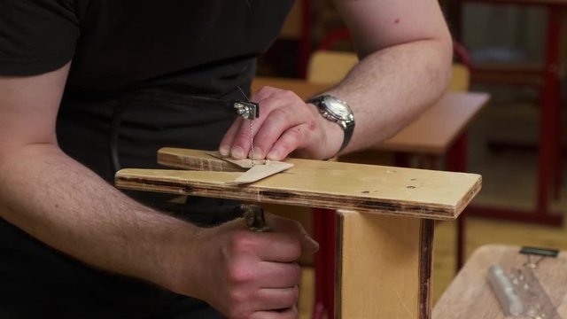 person with wrist watch cuts outdated passenger airplane detail with black fretsaw on brown wooden support slow motion closeup