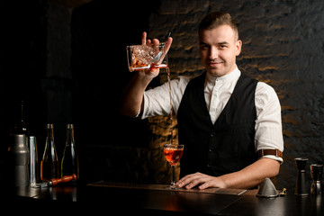 smiling young bartender at bar pours cocktail into glass