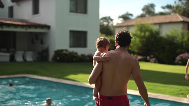 Parent holding baby infant in swimming pool outdoor home garden setting