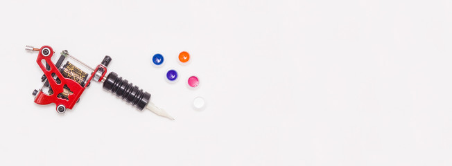 Rotary tattoo machine and color paints in disposable plastic jars on a white background. Free space for text. Banner. The view from the top.