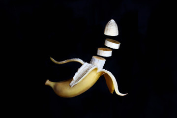 sliced banana with open skin in the tossed state on a dark background