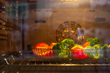 Pieces of broccoli, tomato are in the oven in yellow light. Concept of cooking healthy food.