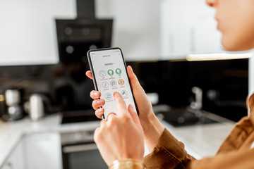 Woman controlling kitchen appliances with a smart phone, close-up on mobile device with launched...
