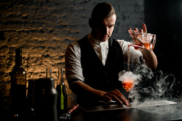 Close-up. Professional bartender pours cocktail to smoky glass