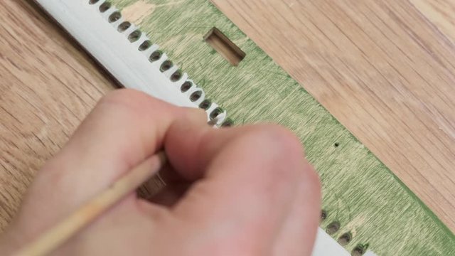 person hand paints wooden outdated plane model fuselage between windows in white with brush on table slow motion closeup