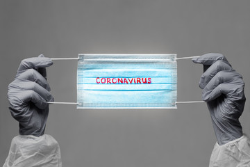 CORONAVIRUS. COVID-19 concept. blue medical face mask with a red inscription CORONAVIRUS in the hands of which are in rubber gloves. vignette image
