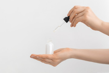 Woman hand holding pipette with collagen moisturizing hyaluronic acid serum in a white light bottle with pipette isolated on grey background.