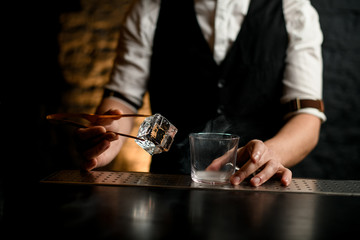 close-up. Bartender holds in hand tweezers with ice near steaming glass