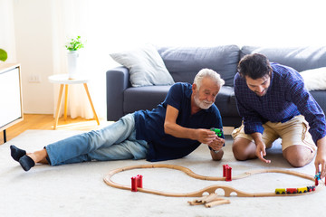 Obraz na płótnie Canvas Father and son family time together at home concept. Bearded olf Father and Bearded middle age Son Playing Toy train on floor at home.
