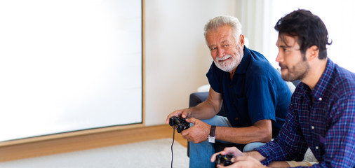 Father and son family time together at home concept. Happy father and son enjoy playing video games with joysticks in living room at home