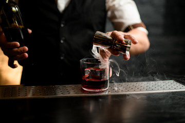 close-up. Barman's hand pours smoky drink from jigger into glass with ice