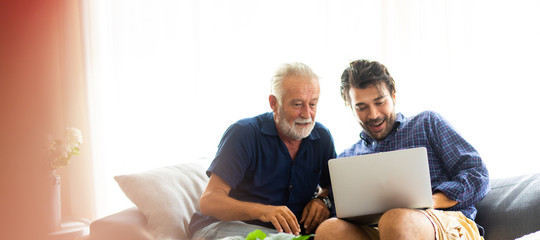 Father and son family time together at home concept. Smiling old father and happy son sitting on sofa using digital laptop computer in living room at home