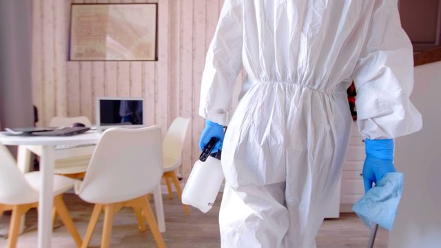 A person with protective suit and chimical disinfectant in a house
