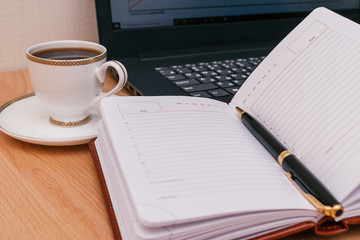 Notebook with a pen,laptop,white cup of coffee and on the wooden table.Concept work from home.Remote work due to the coronavirus pandemic.Top view,copy space for text