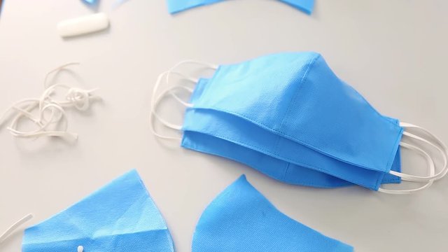Smooth movement of the camera on the table for cutting and sewing, changing focus from the unfinished mask to the finished masks and to the scissors lying on the blue cloth. Concept of sewing masks.
