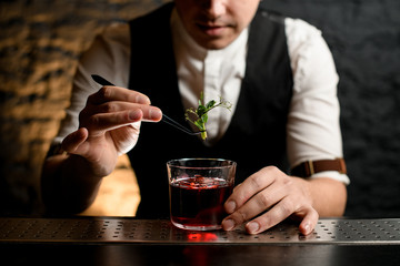Close-up of glass with drink which bartender accurate decorating with fresh green plant.