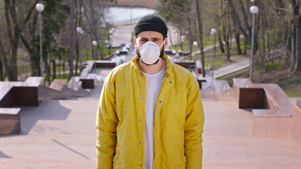 Young man in a yellow jacket and hat wearing his protective mask while standing on the park stairs new Covid-19