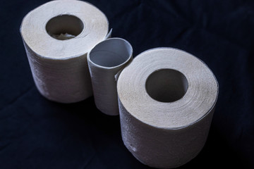 Three rolls of single-layer and thin toilet paper on a black background, two whole rolls