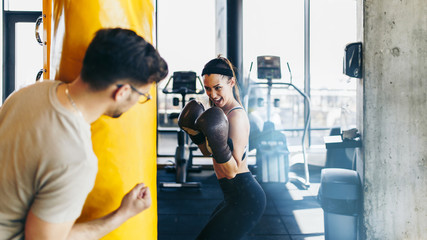 Young attractive woman with instructor on kickboxing training. She hitting or punching in big yellow boxing bag.