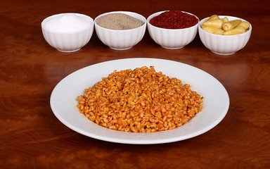 Cooked oatmeal with delicious tomato sauce ready to serve on a white plate with special Turkish spices on a wooden table