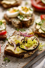 Fototapeta na wymiar Vegetarian open sandwich with buckwheat bread, grilled zucchini slices and red onion on a wooden board close up view