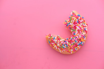 Half eaten donut on pink background 