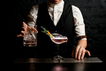 Close-up male bartender holding glass mixing cup and decorated glass vessel in shape of bird stands nearby