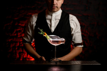 Close-up. Beautiful exclusive glass vessel in shape of bird with drink and decorated with plants stands on bar.