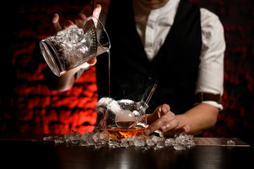 Close-up professional bartender pours cold drink into designer flask