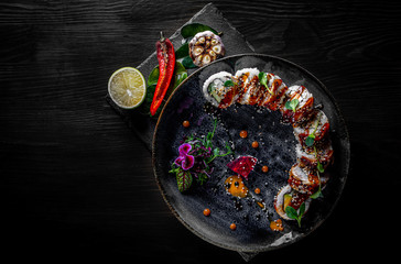 sushi roll with cream cheese, cucumber and eel in plate on black wooden table background
