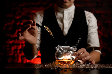 close-up bartender decorate with spikelet designer flask with alcoholic drink