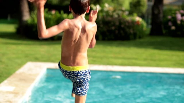 Young boy jumping into swimming pool water outdoors