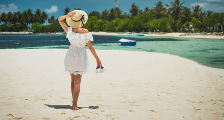 A girl in a hat and white dress is walking along the beach. White sand beach. Maldives, island of Guraidhoo. Girl on vacation. Paradise beach.