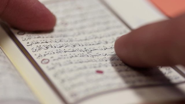 A person is reading from a small Quran and tracing the versions with the finger...