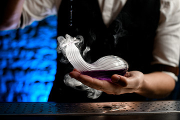 Fototapeta premium Close-up of smoky glass flask of unusual shape in bartender's hand