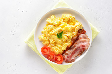 Scrambled eggs, fried bacon and tomatoes on plate