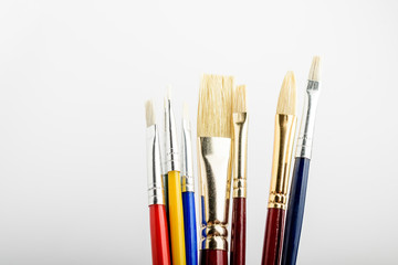 Many professional artist paintbrushes displayed vertically isolated on a white studio paper, photographed with soft focus
