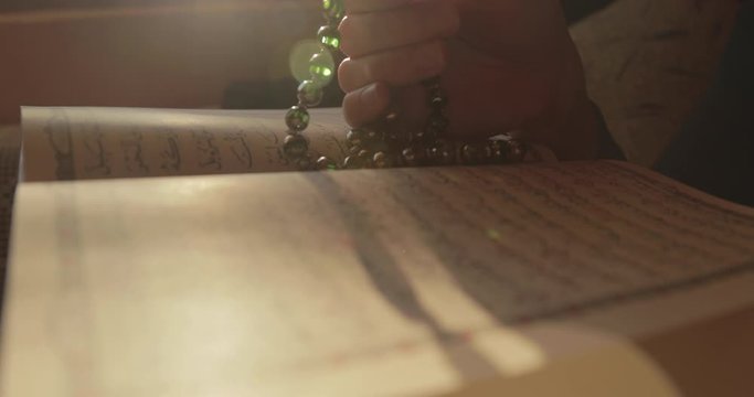 A person praying dhikr on the Muslim prayer beads with an opened Quran in the front...