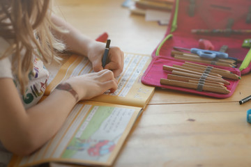 young blonde left-handed girl is writing in a workbook to train her handwriting at home - homeschooling concept - Powered by Adobe