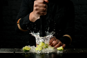 Close-up. Bartender holds madler and energetically squeeze slices of citrus to cocktail