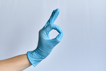 A hand in a medical blue glove on a white background shows a good signal or OK.
