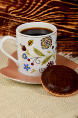 decorated small cup full of black coffee next to one chocolate cookie